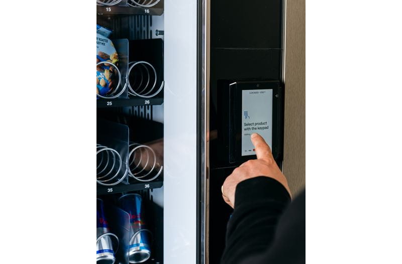 Máquina vending con el dispositivo desatendido y el dedo de una persona tocando la pantalla.