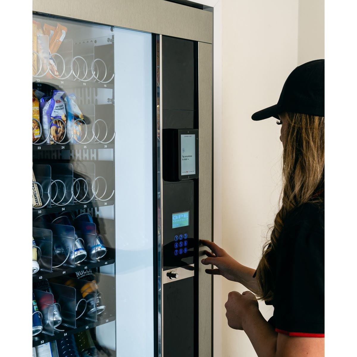 Chica observando la máquina vending y mirando la pantalla para seleccionar el número del producto que desea.